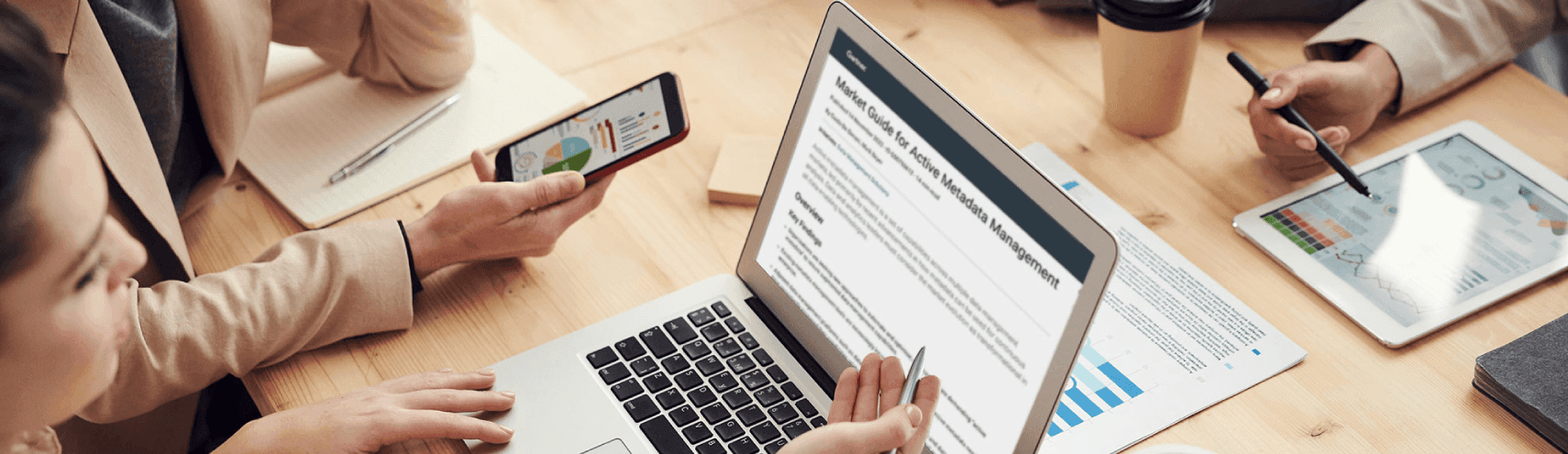 Alation Blog Image: Group gathered around a conference table in an office setting with their laptops, cellphones, tablets, and sticky paper taking notes while discussing what is active metadata and why it matters.