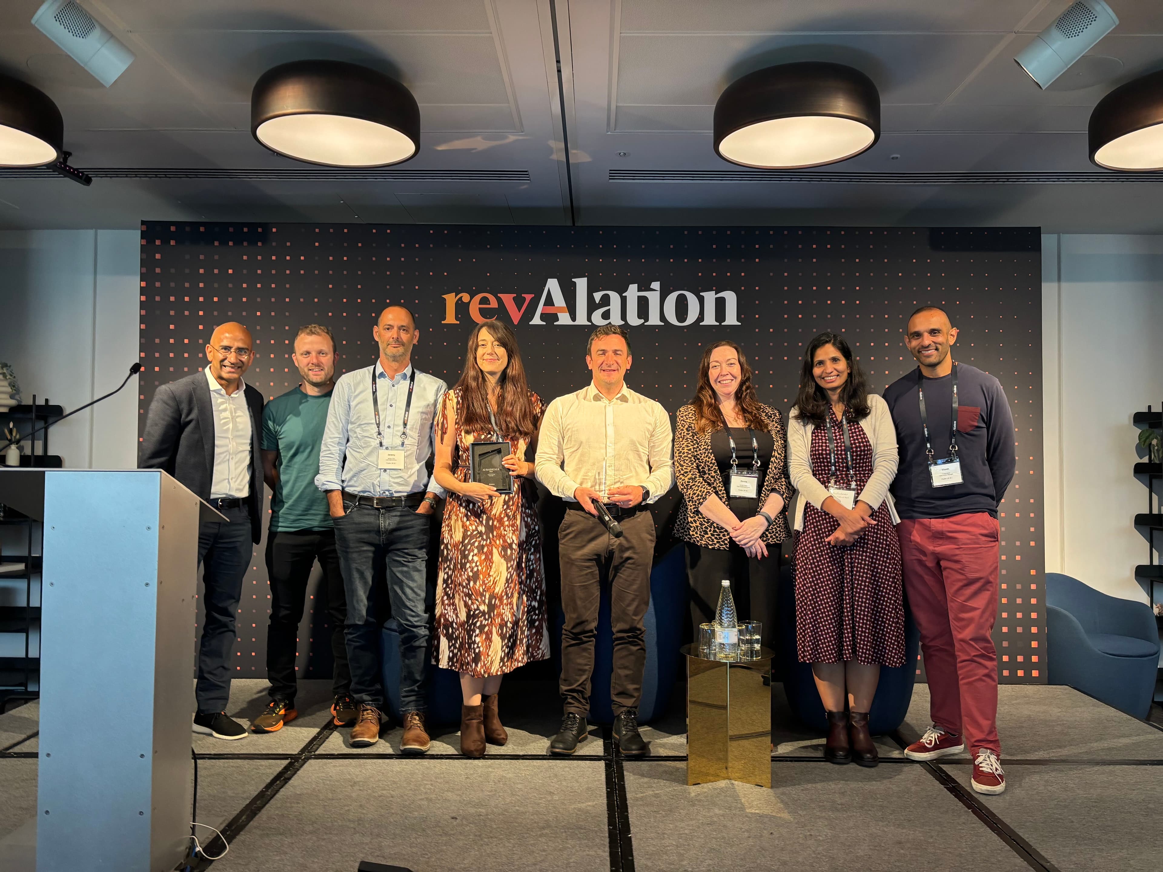 Eight people posing on stage at the revAlation event, with two holding awards, smiling in front of a branded backdrop.