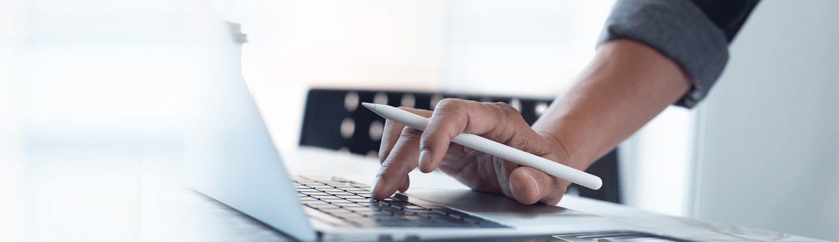 Focus shot of a hand holding an Ipad pencil while hovering over an opened laptop