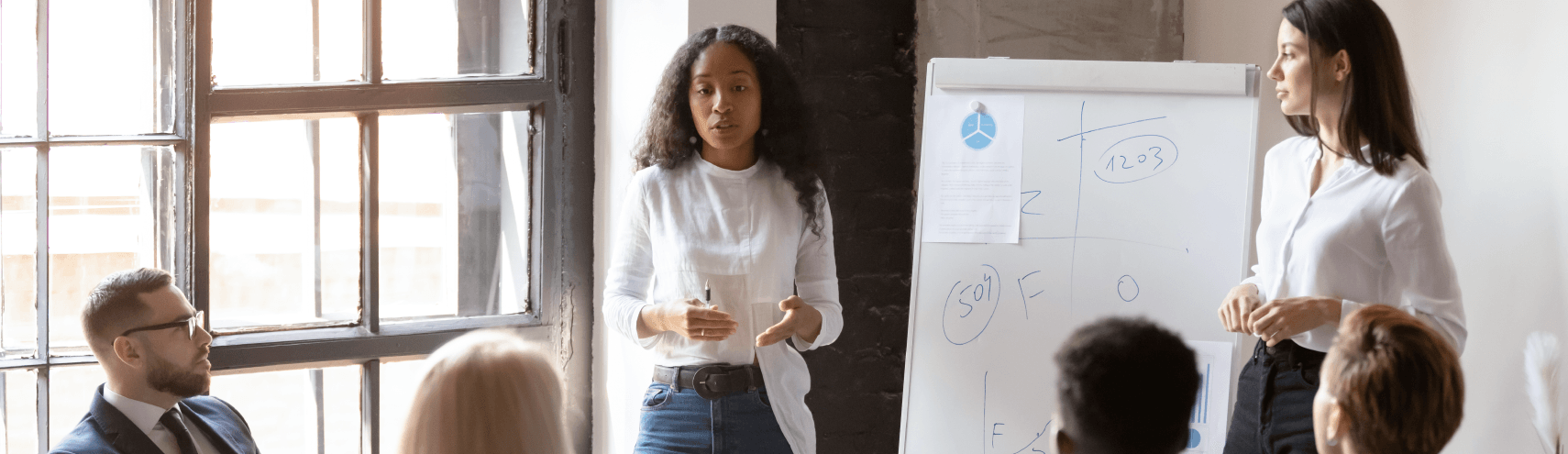 Alation image: Two business women diving into strategies for implementing a data catalog to a group of coworkers