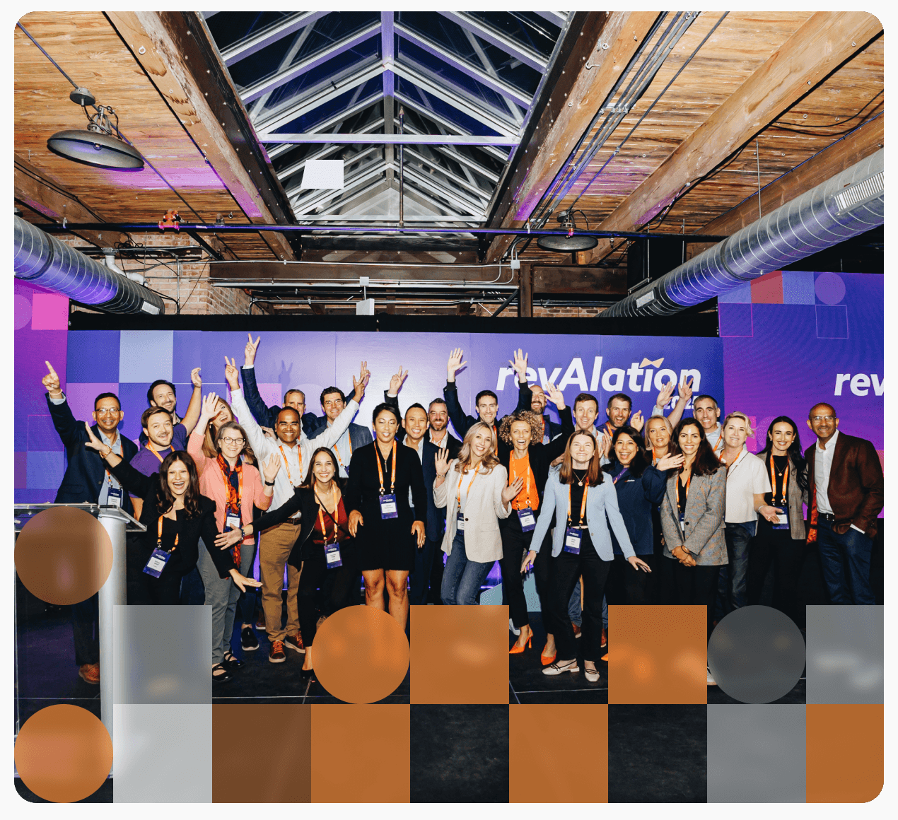 Group of professionals posing with raised hands at a revAlation event, under industrial ceiling with purple lighting.