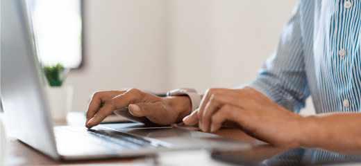 Alation blog image: Close-up of a person's hands typing on a laptop keyboard, situated on a desk with a blurred background, suggesting a home or office setting.