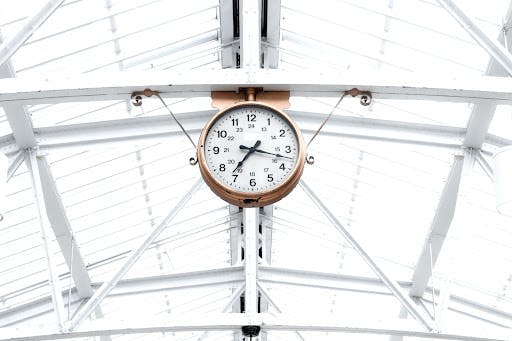 A vintage golden clock hanging from the white ceiling of a train station or mall.