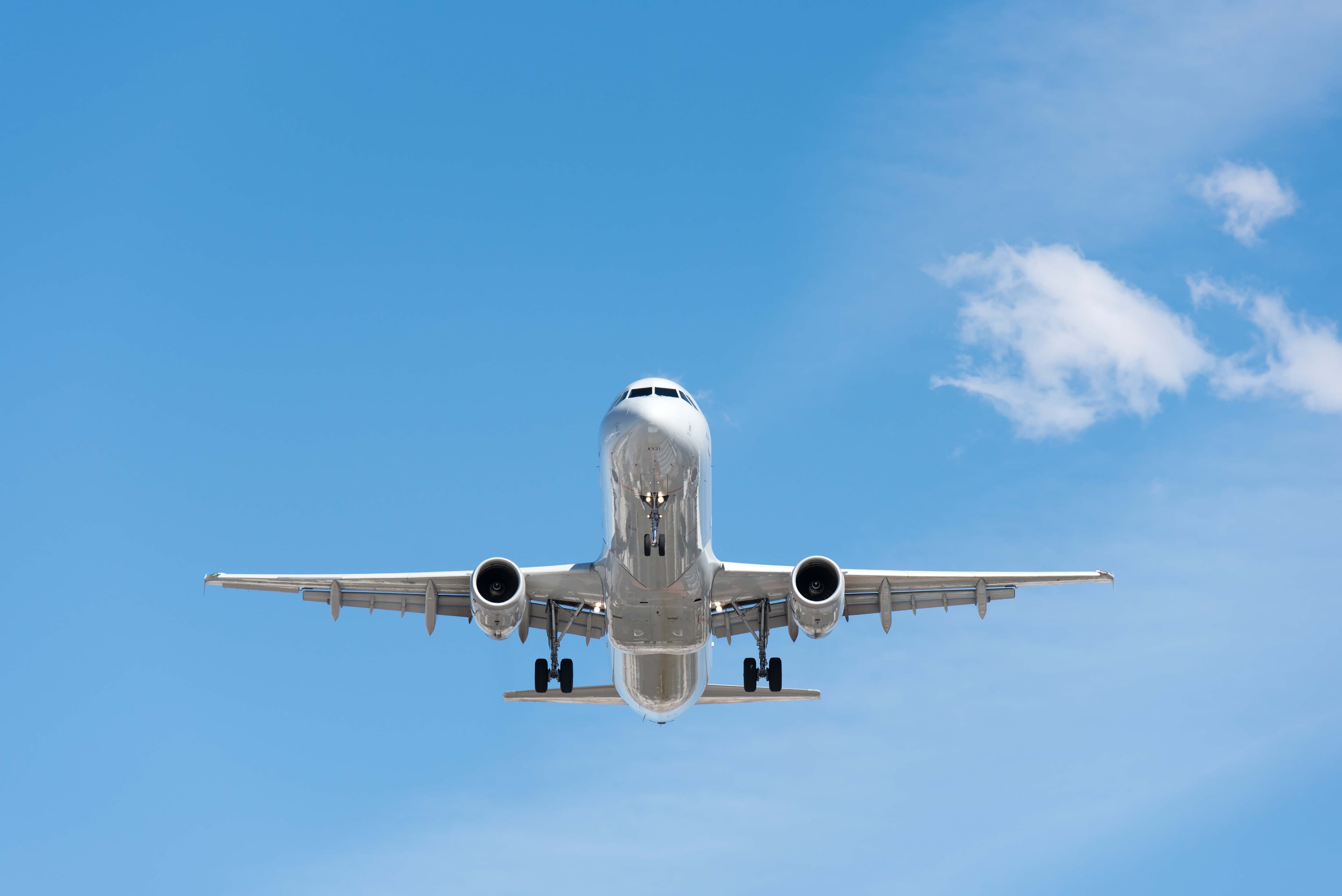 White passenger airplane flying directly overhead against a clear blue sky with a few wispy clouds.