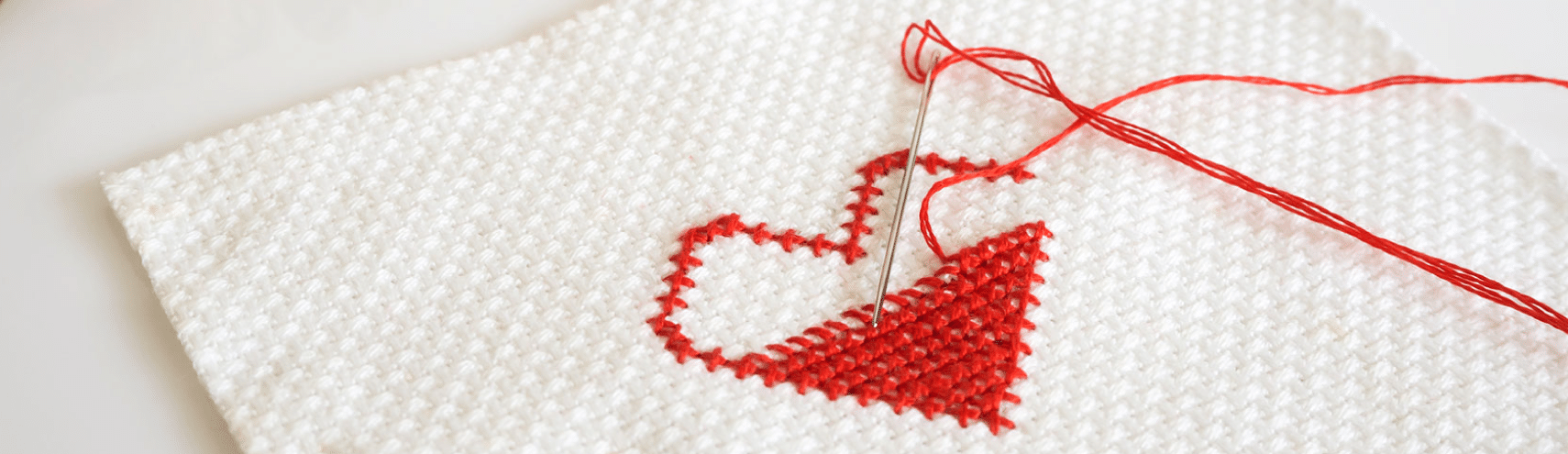 Stitching of red heart halfway completed on a white fabric with multicolored threads behind it