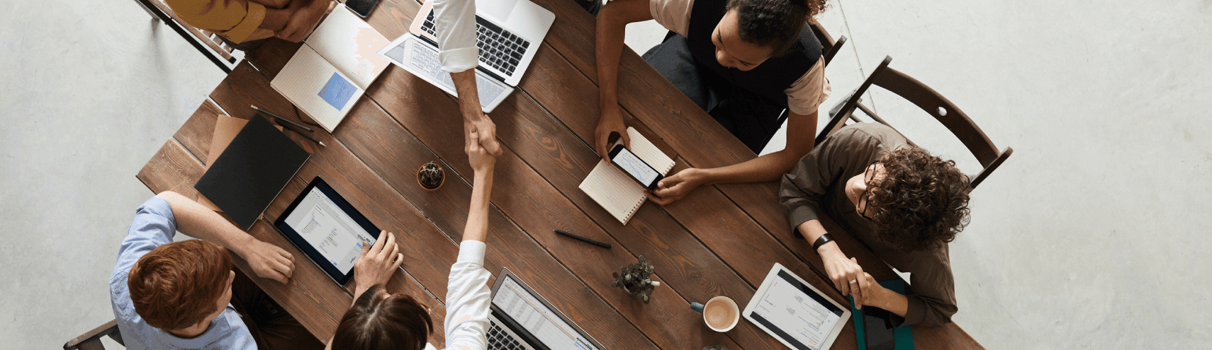 Birdseye view shot of a corporate meeting taking place as someone handshakes another person's hand indicating a partnership