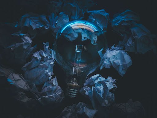 A light bulb fixture surrounded by crushed notepad papers in a dark background