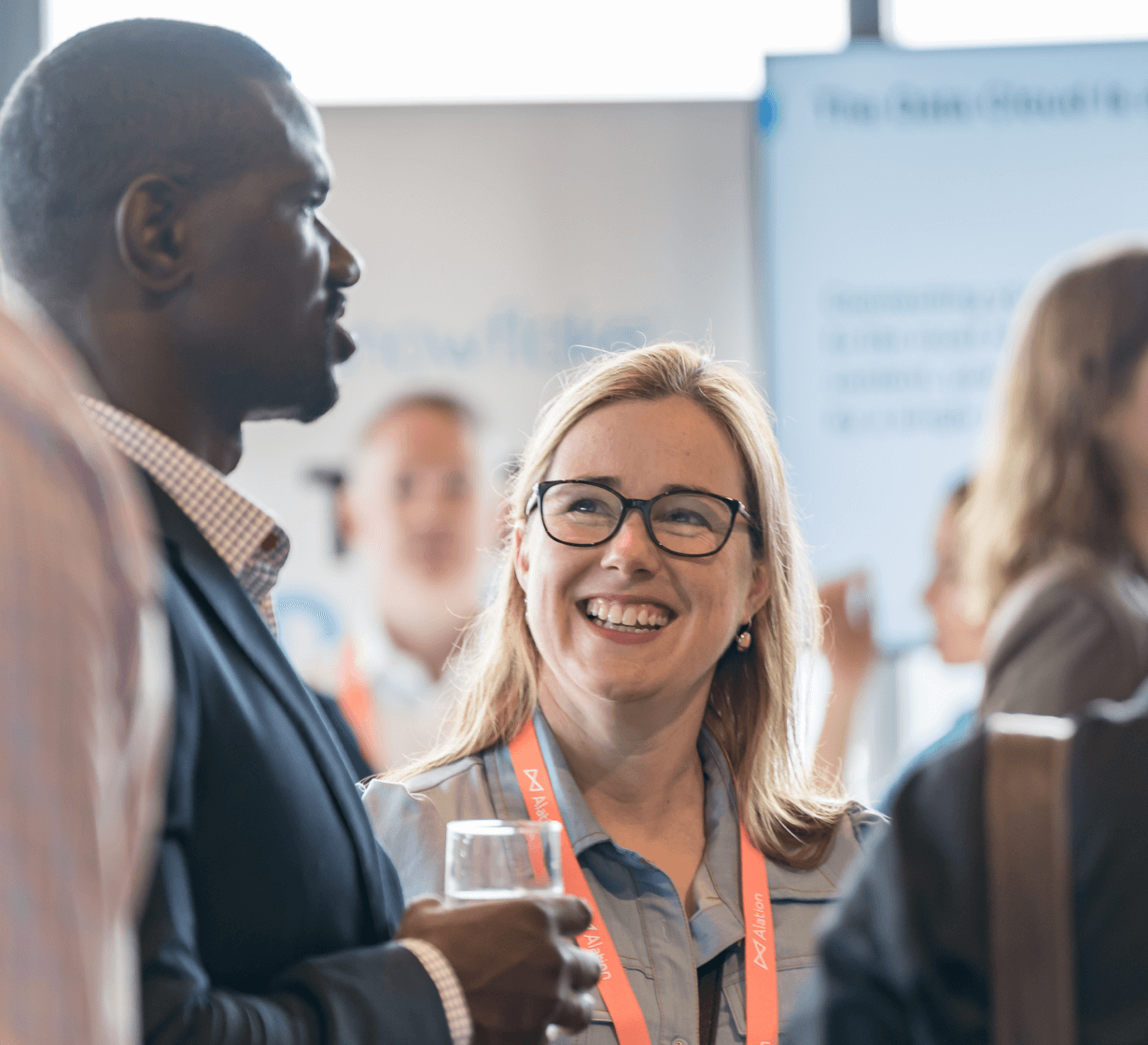 Diverse professionals networking at a conference, woman with glasses smiling while conversing with colleagues.
