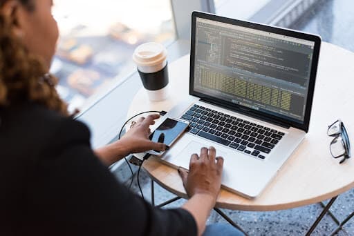 Top-down view of a person analyzing data quality metrics on a laptop, with a smartphone resting on the laptop, accompanied by glasses and a coffee cup on the desk.
