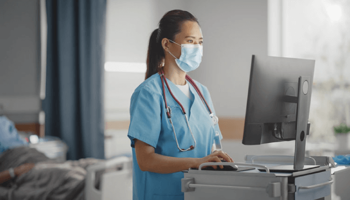 A nurse using a mask and scrubs while working on a computer.