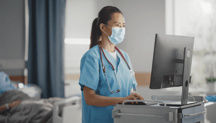 Alation Blog Image: A nurse using a mask and scrubs while working on a computer.