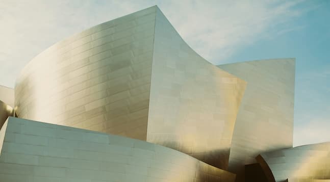 Curved, gleaming stainless steel panels of a modern building against a pale blue sky, showcasing bold, flowing architectural design.
