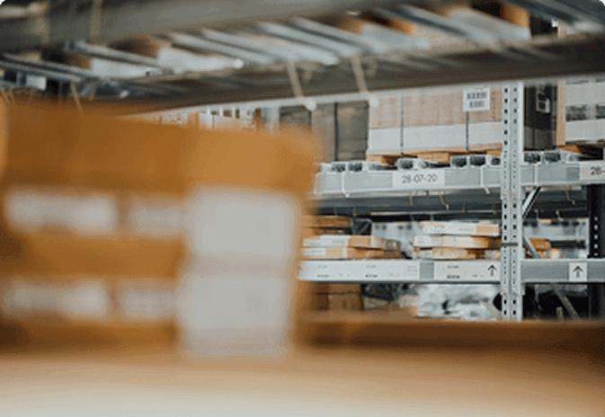 Warehouse shelves stocked with labeled cardboard boxes and packages, with a blurred box in the foreground.
