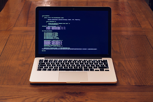 An open laptop on a wooden table displaying a programming environment with code on a dark blue background.