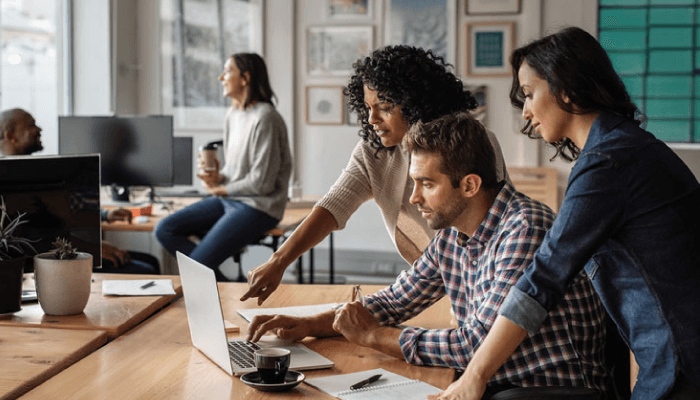 Alation Blog Image: A group of coworkers gathered around a laptop together in an opened office space.