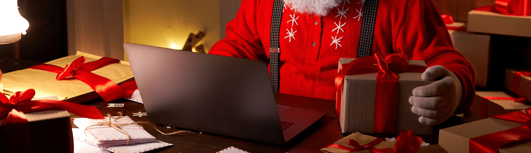 Santa sitting on his desk with a laptop, gift box, and packaging envelopes.