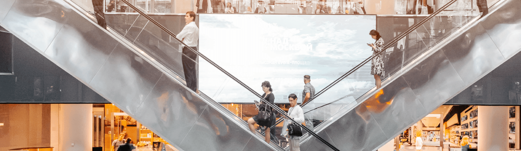 Two escalators with people going up and down in the middle of a retail mall