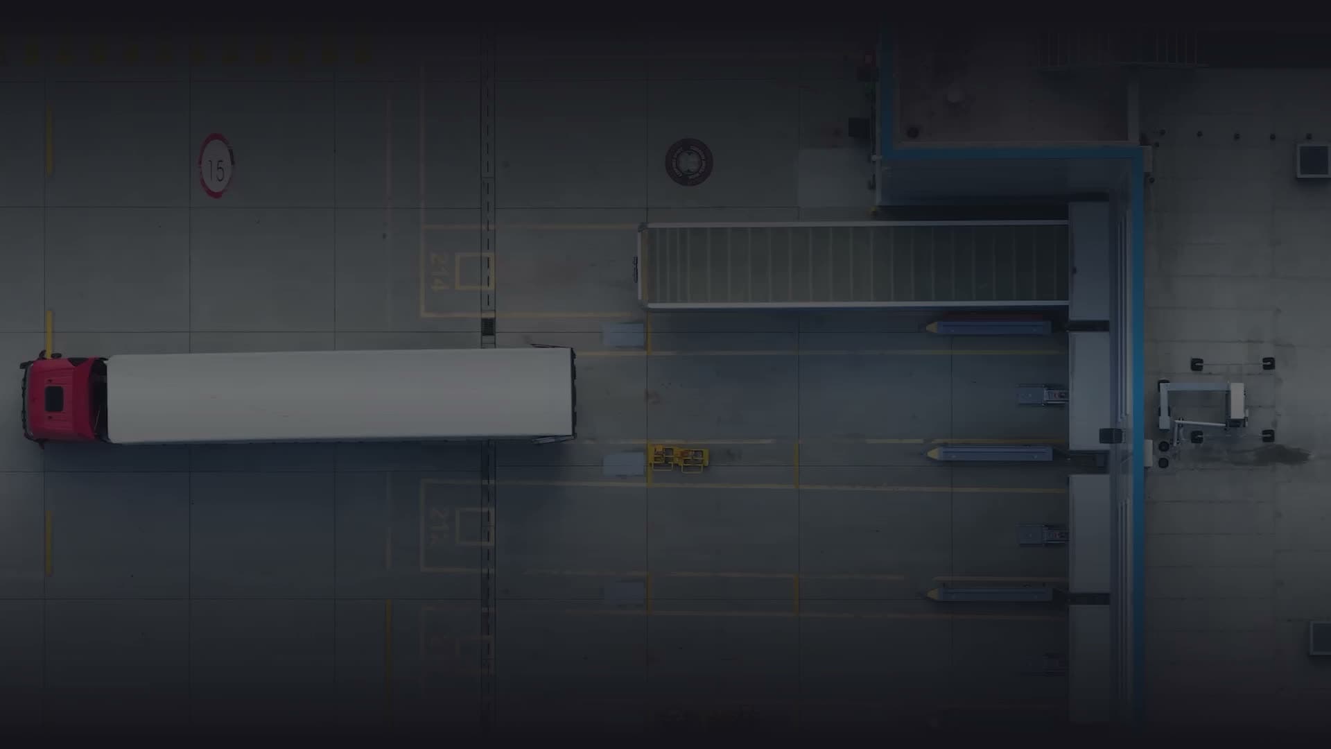 Aerial view of a logistics facility with a red semi-truck and white trailer parked near a warehouse loading dock.