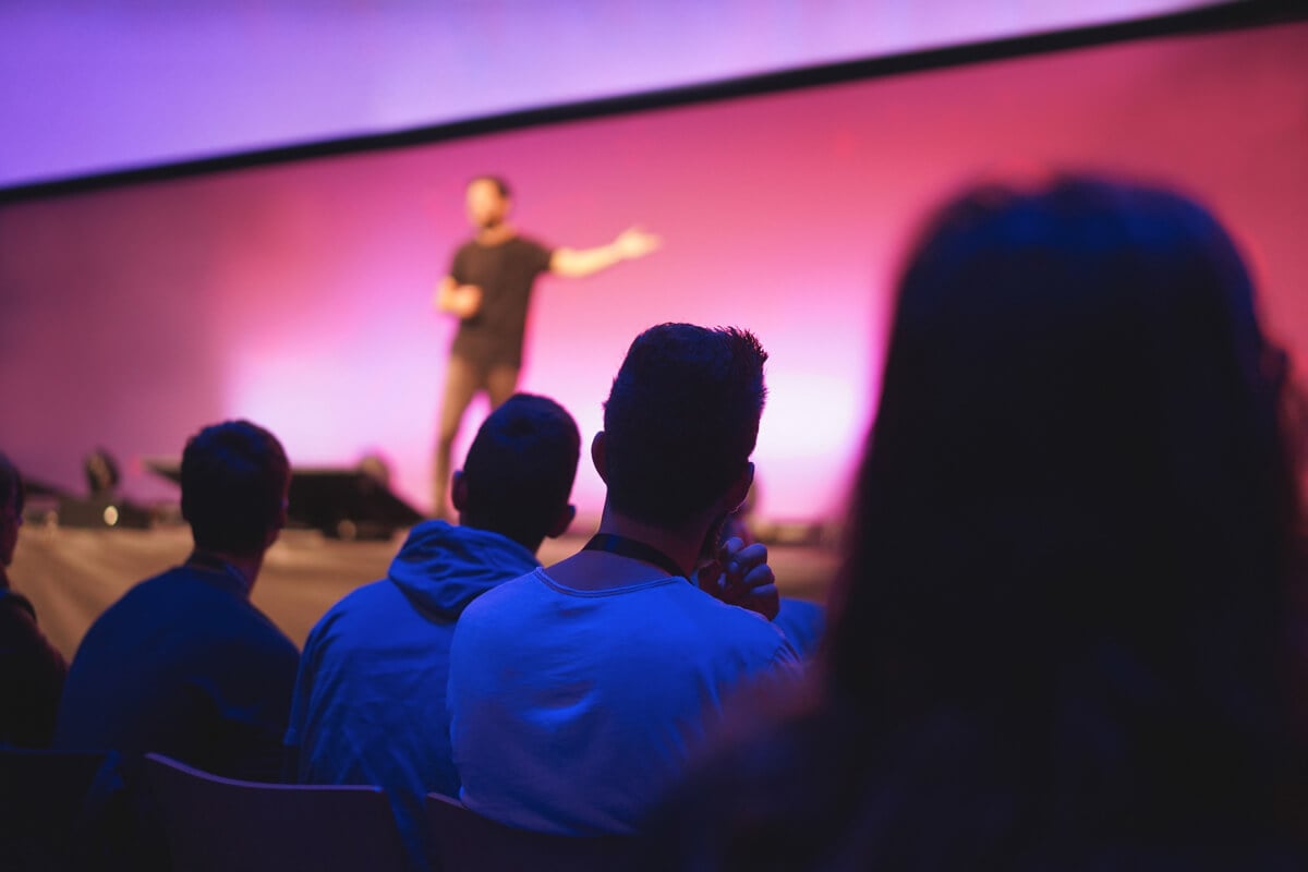 Alation Blog Image: speaker speaking in front of a pinkish background in front of an audience.