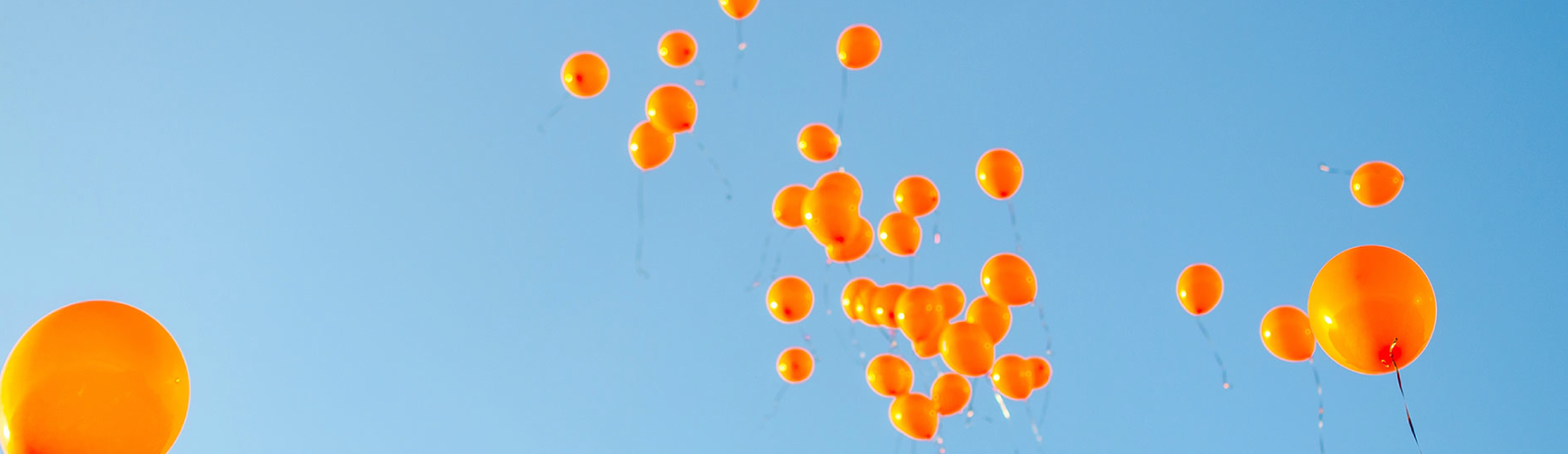 Orange balloons flying through a blue sky.