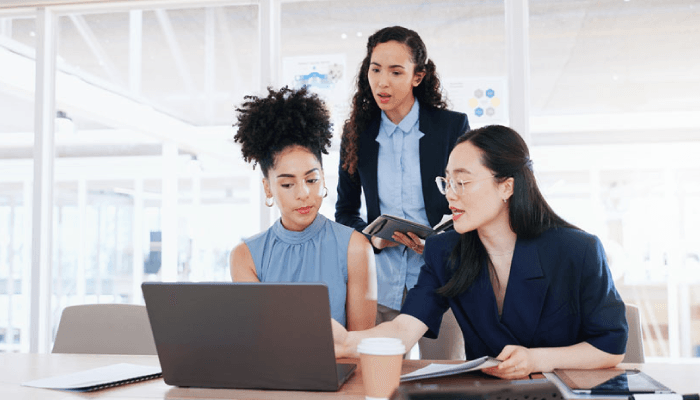 Alation Blog Image: Three business women in an office space with their opened laptops reviewing what is data compliance together.