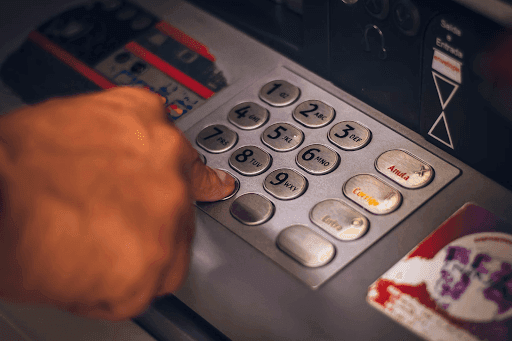 Close-up of a person's hand pressing a number on an ATM keypad.