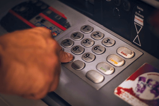 Close-up of a person's hand pressing a number on an ATM keypad.