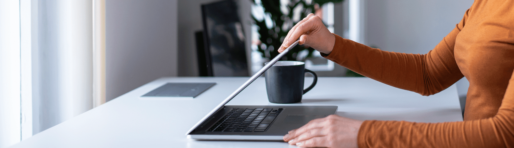 Woman in her home office opening up her laptop wearing a orange turtleneck sweater