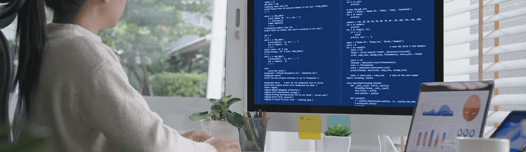 A Data Engineer working from home with her laptop and desktop monitor opened with charts of data being displayed