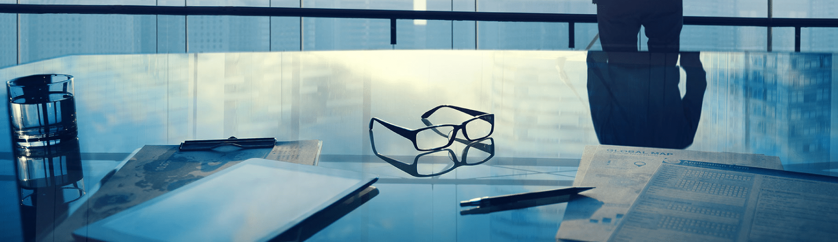 Office space focusing on reading glasses on table with man in background looking at the horizon.