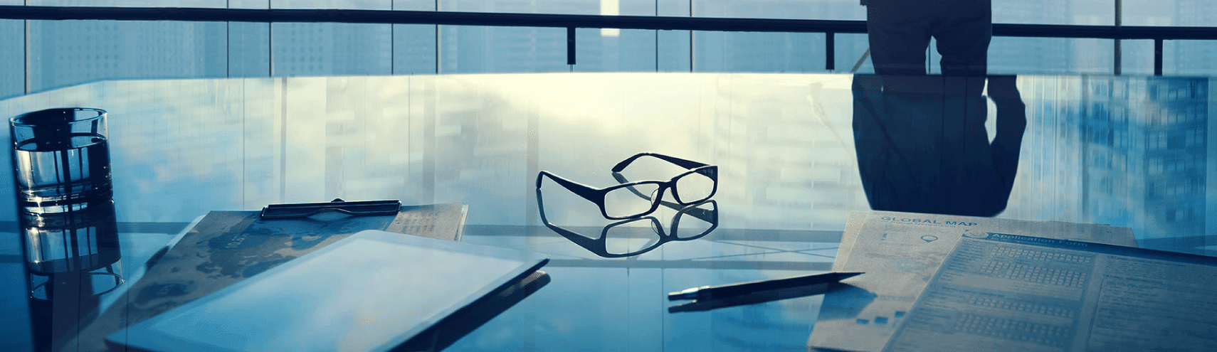 Office space focusing on reading glasses on table with man in background looking at the horizon
