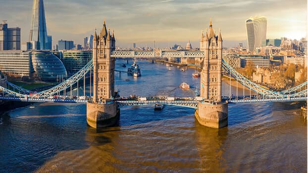 London skyline featuring Tower Bridge spanning the Thames River with The Shard and Walkie-Talkie buildings visible at sunset.