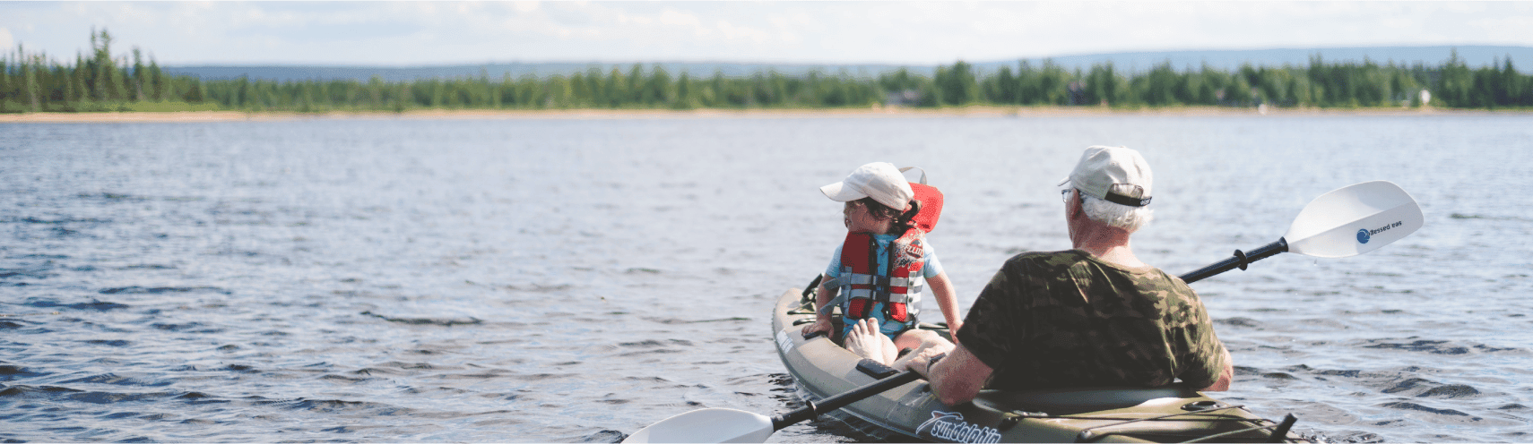 A grandfather and his grandson are kayaking on a lovely sunny day