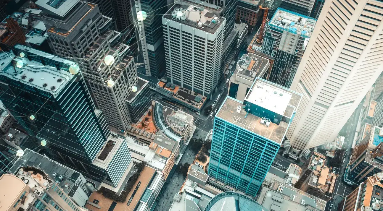 Aerial view of a dense city skyline with skyscrapers and a digital network overlay of glowing nodes and lines.