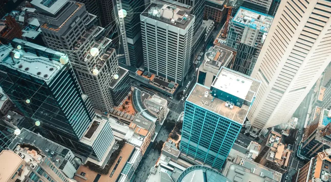 Aerial view of a dense city skyline with skyscrapers and a digital network overlay of glowing nodes and lines.