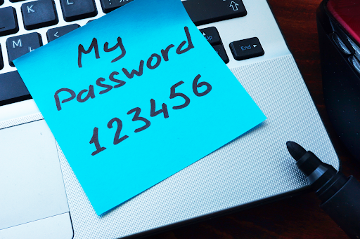 A sticky note with 'My Password 123456' written on it, placed on a laptop keyboard next to a marker, highlighting poor password security practices.