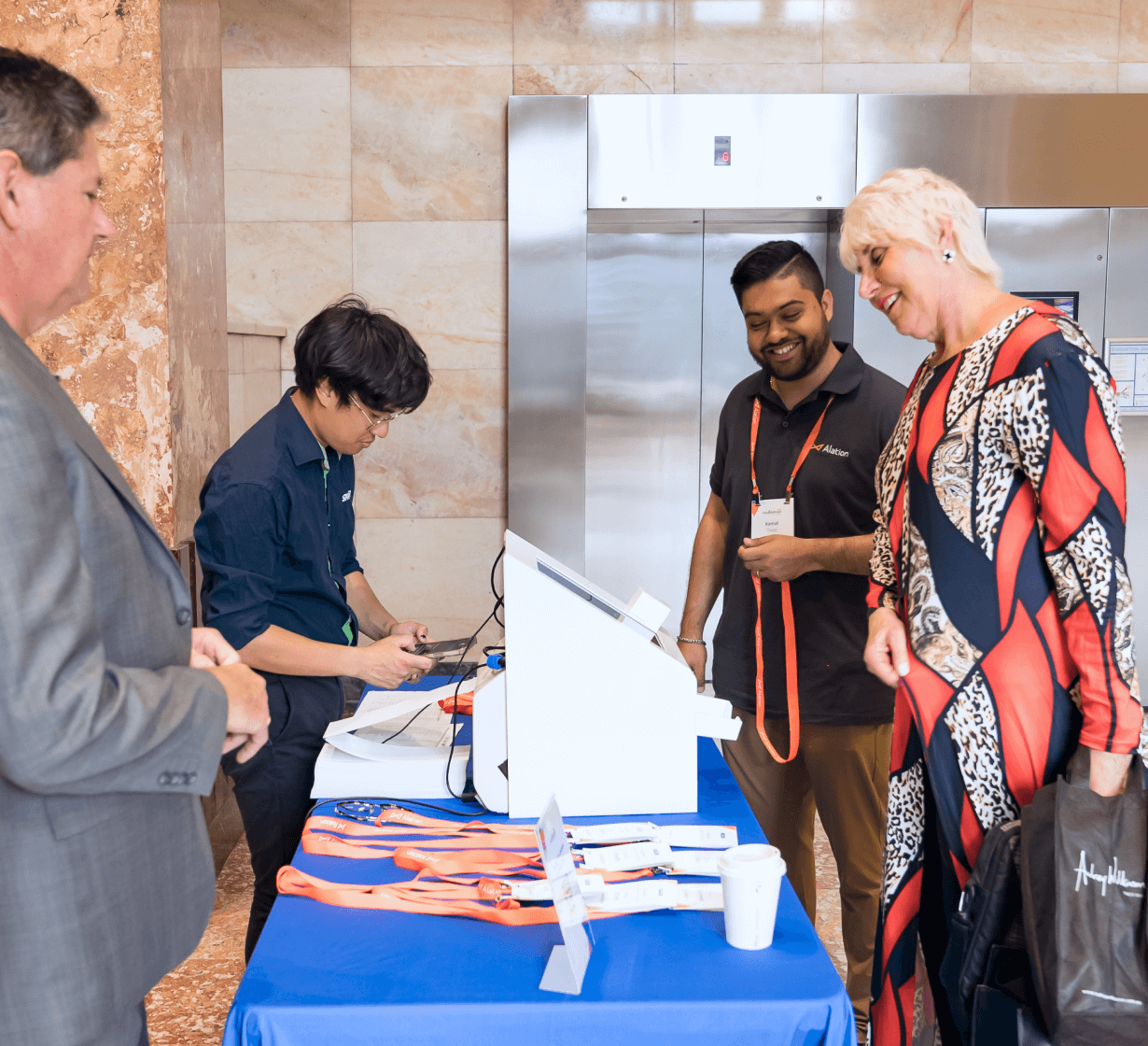 Four people at a conference registration table with orange lanyards and name badges on a blue tablecloth.