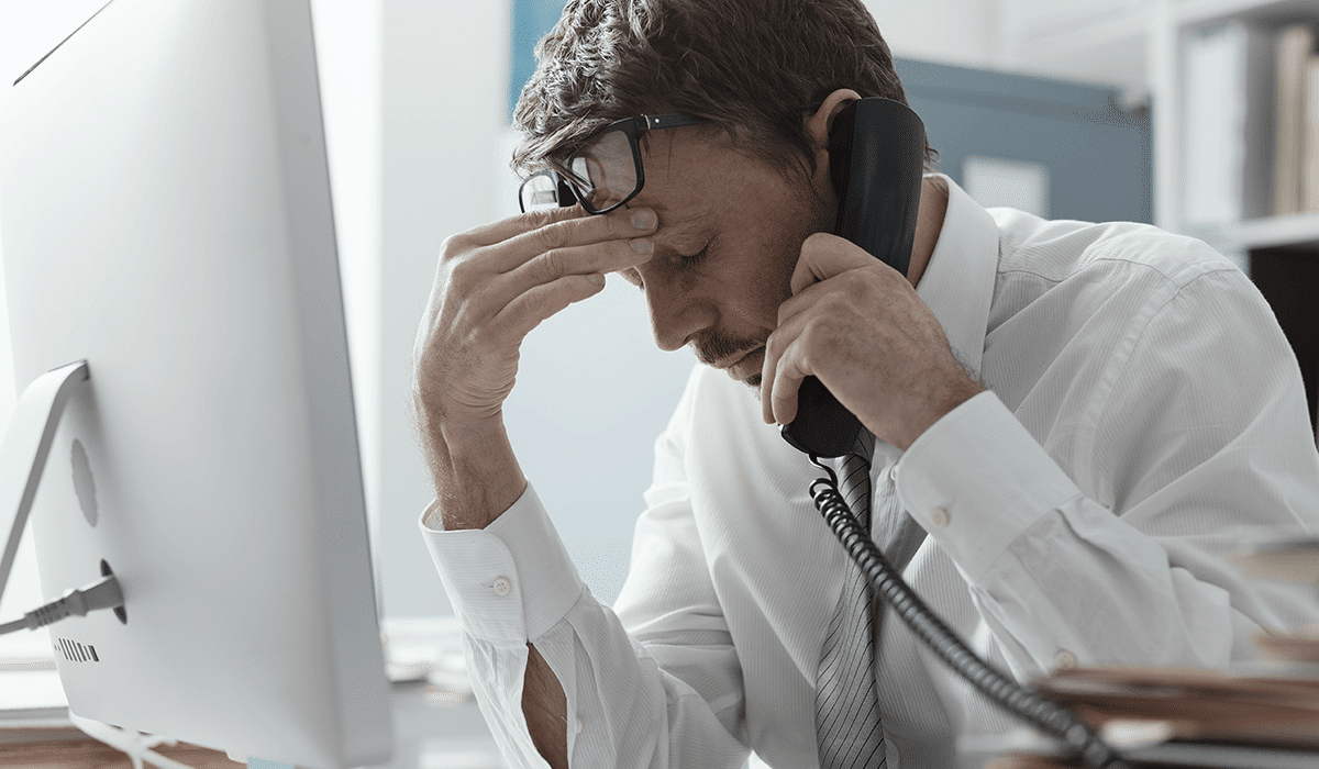 A stressed business man, scrunching his forehead, on the phone in an office setting.